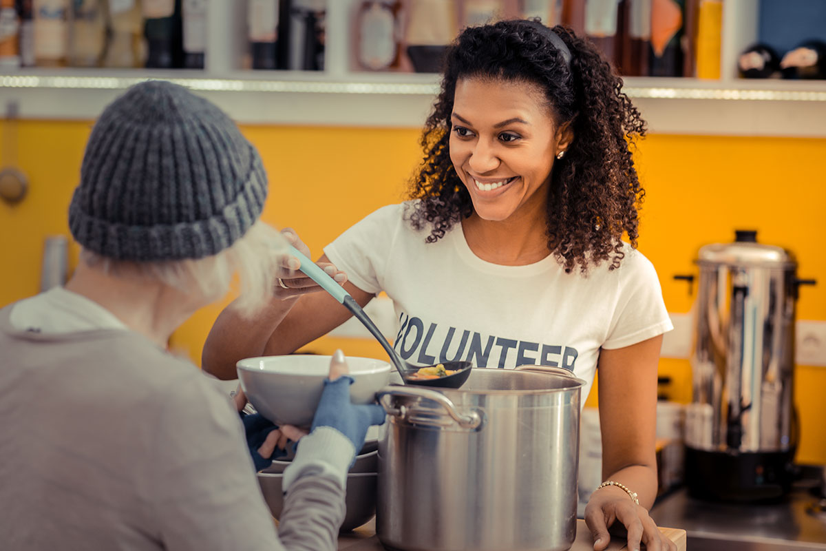 A volunteer serving a bowl of soup to a person in a wooly hat